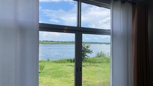 Una habitación con un amplio ventanal con vistas a un lago y un espacio cubierto de césped.