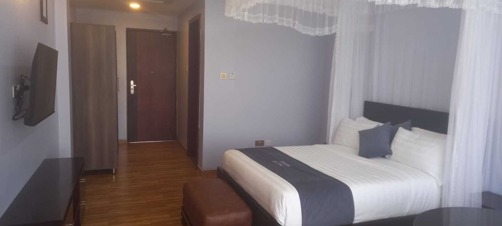 Una habitación de hotel con una cama, un banco, un televisor y una puerta que da a otra habitación.