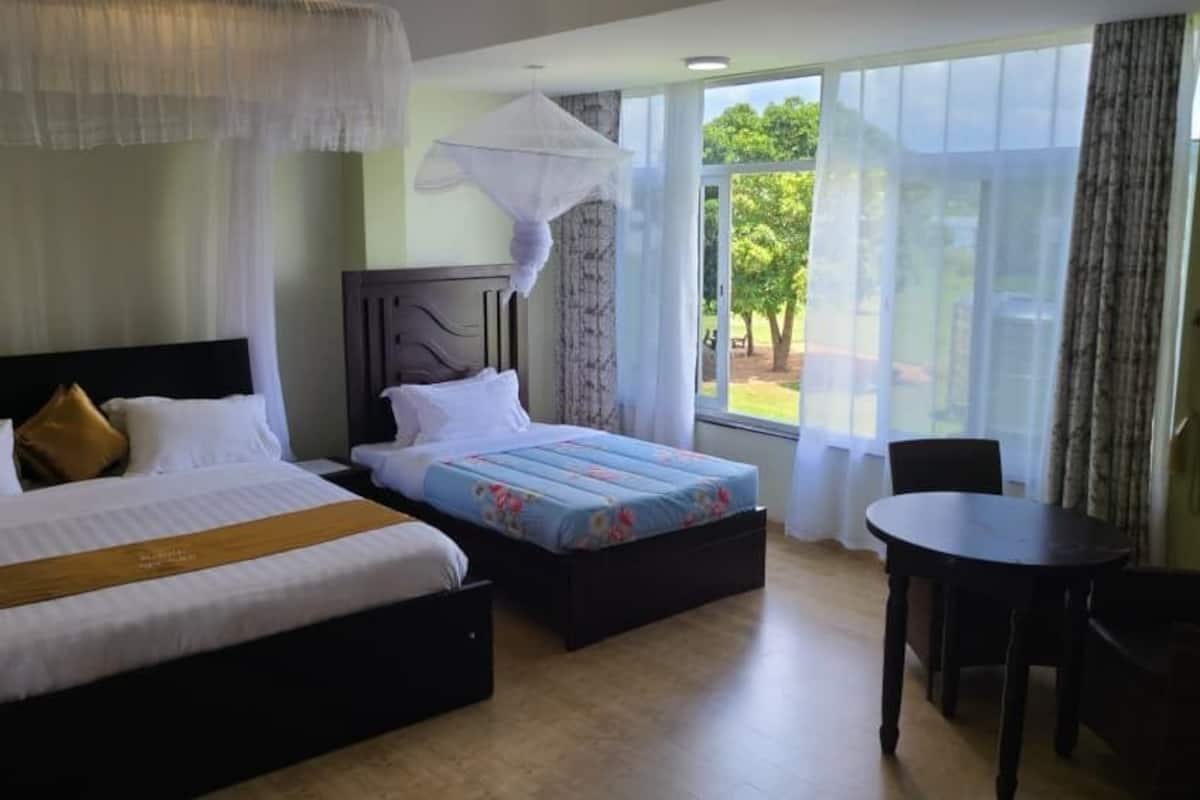 Ein Hotelzimmer mit einem großen Bett, einem kleineren Bett, einem Esstisch und Blick ins Freie.