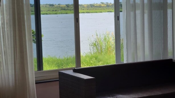Habitación con un ventanal grande que da a una masa de agua y vegetación.
