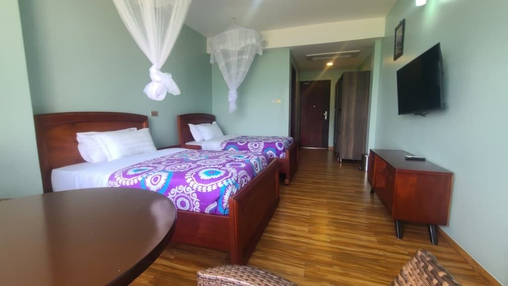A hotel room with two beds, a wooden floor, a TV, and a desk.