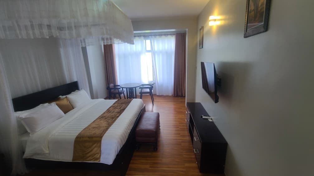 A hotel room with a bed, a desk, a chair, a TV, and a window with curtains.