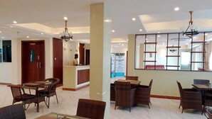 Un vestíbulo de hotel con varias zonas de estar, un mostrador de recepción y un panel informativo en la pared.