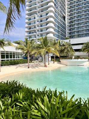 Un hôtel moderne doté d’une piscine, de palmiers et d’une plage de sable.