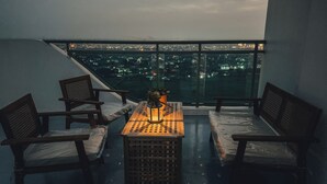 A balcony with a table, chairs, and a view of the city at dusk. - Luxury Penthouse in CBD w/ Wave Pool, 7ft Billiards & Wide Balcony for Getaways (San Fernando)