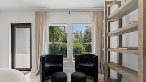 Ein modernes Zimmer mit zwei schwarzen Stühlen, einer Holzbibliothek und Blick auf Grün hinter großen Fenstern.