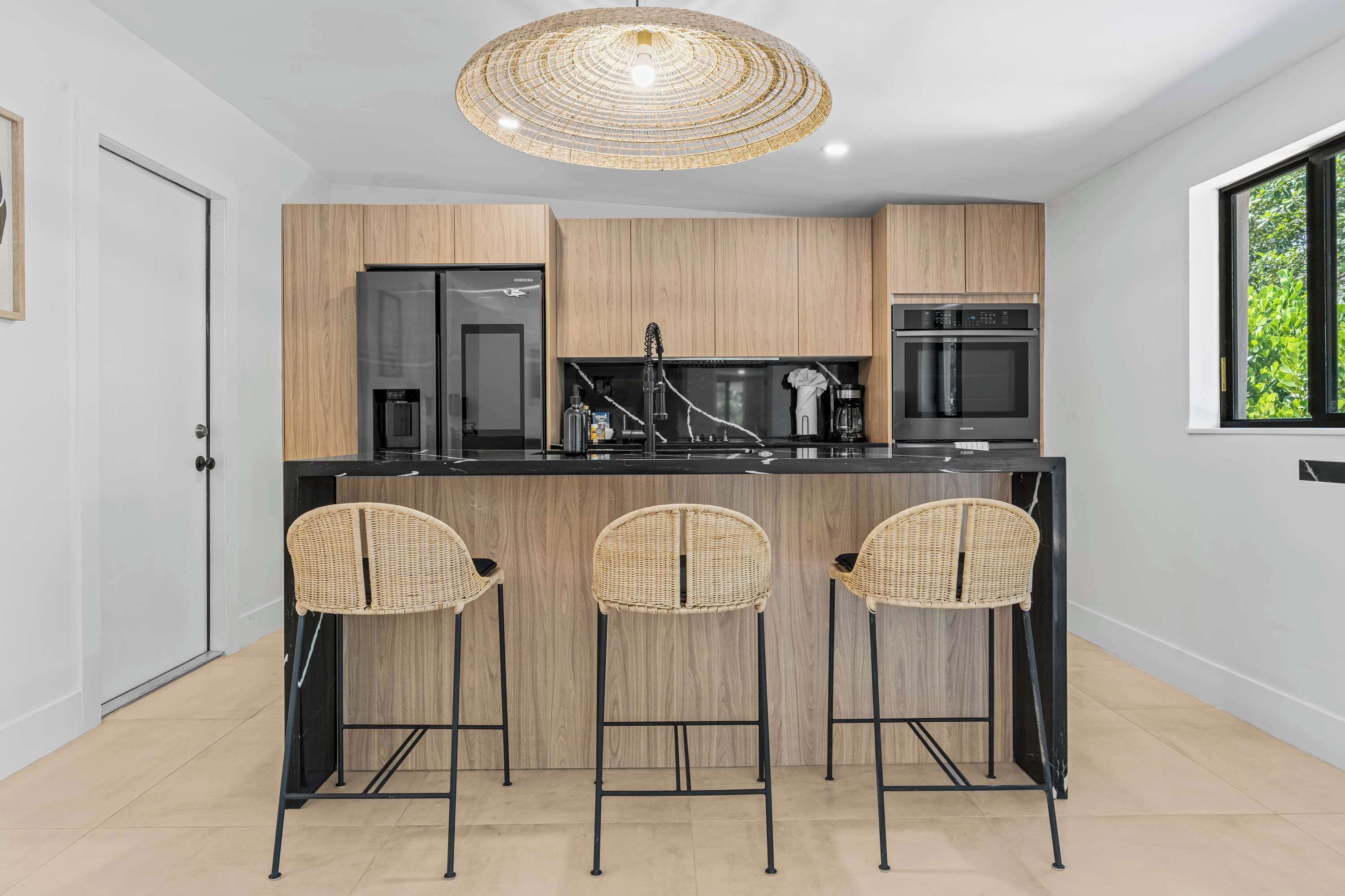 A modern kitchen with a central island, black appliances, and wicker bar stools.