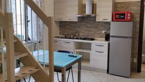 Une cuisine compacte équipée d’une cuisinière à gaz, d’un four à micro-ondes et d’un réfrigérateur. On y trouve également une table à manger avec des chaises.