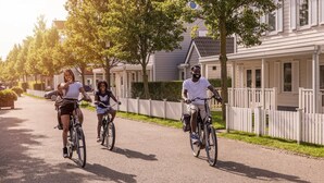 A residential street with houses, a white picket fence, and a clear sky.