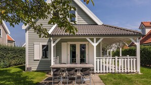 A house with a covered porch, a dining table with chairs, and a white picket fence.