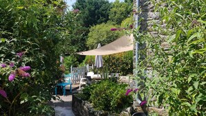 A garden area with a stone wall, a wooden deck, and outdoor seating. - Comfortable gite in the beautiful Brittany countryside (Bignan)