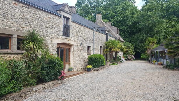 A stone house with a gravel driveway, surrounded by lush greenery and a small garden. - Comfortable gite in the beautiful Brittany countryside (Bignan)