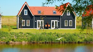 A two-story house with a red-tiled roof and black siding, located beside a calm water body.
