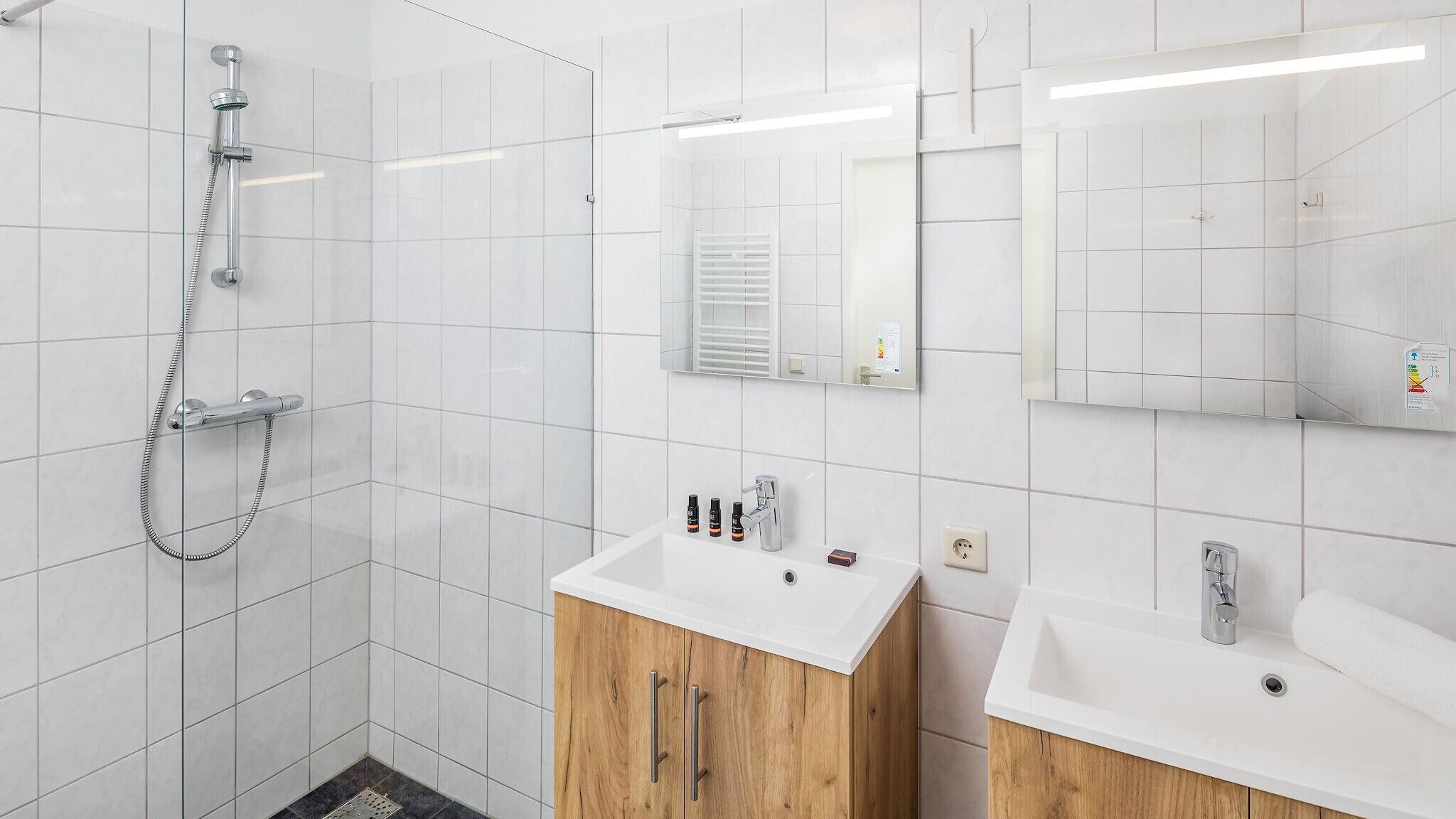 A modern bathroom with a shower, two sinks, and wooden cabinets.