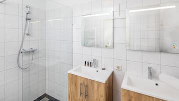 A modern bathroom with a shower, two sinks, and wooden cabinets.