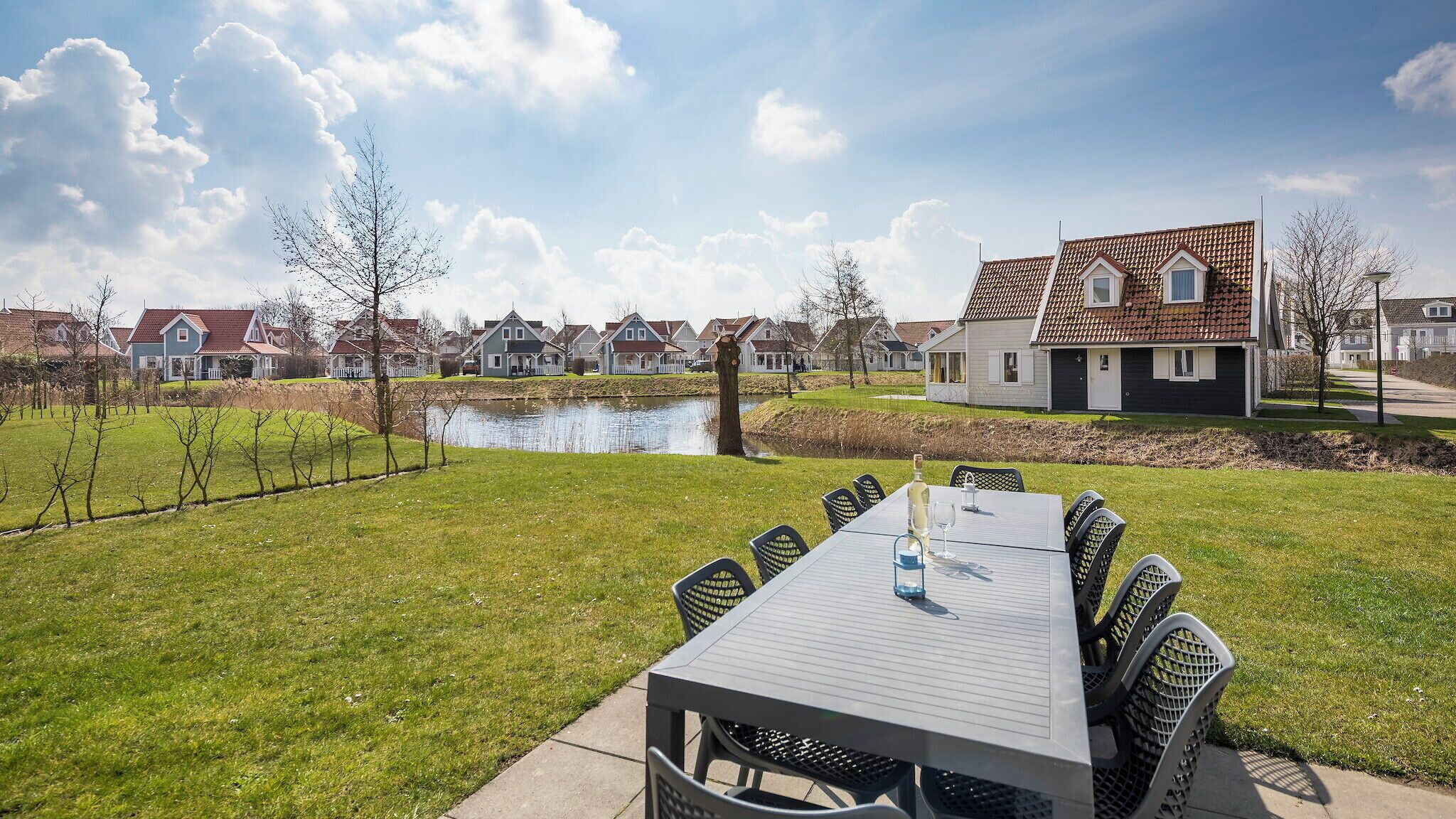 A patio with a table and chairs, a pond, and houses in the background.