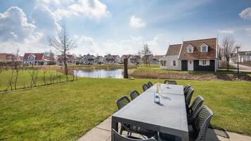 A patio with a table and chairs, a pond, and houses in the background.
