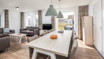 A modern living room with a sofa, coffee table, dining table with chairs, and a TV.