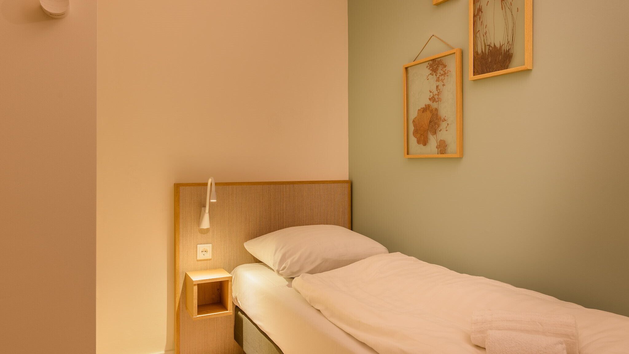 Una cama individual con cabecera de madera, una mesita de noche y una lámpara de pared.