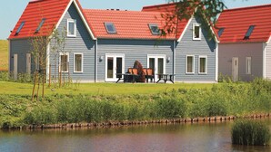 A two-story house with a red roof, a front door, and a patio with outdoor furniture. - Modern apartment for 6 persons (Hageweg 'T Centrum)