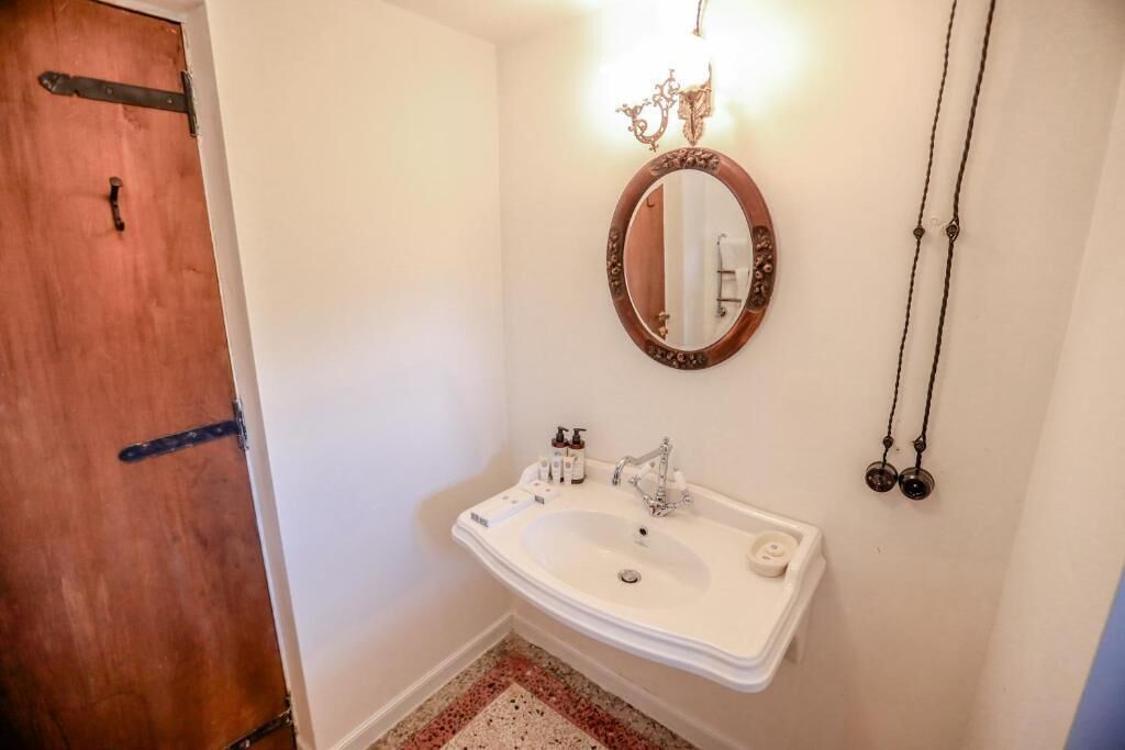Un baño con un lavamanos blanco, un espejo y una puerta de madera.