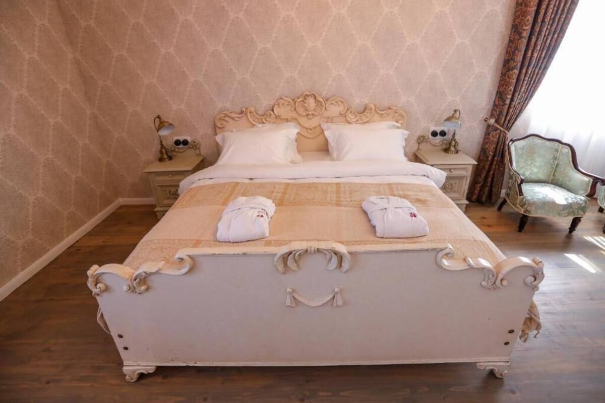 Una cama con un cabecero decorado, dos mesitas de noche con lámparas y una silla.