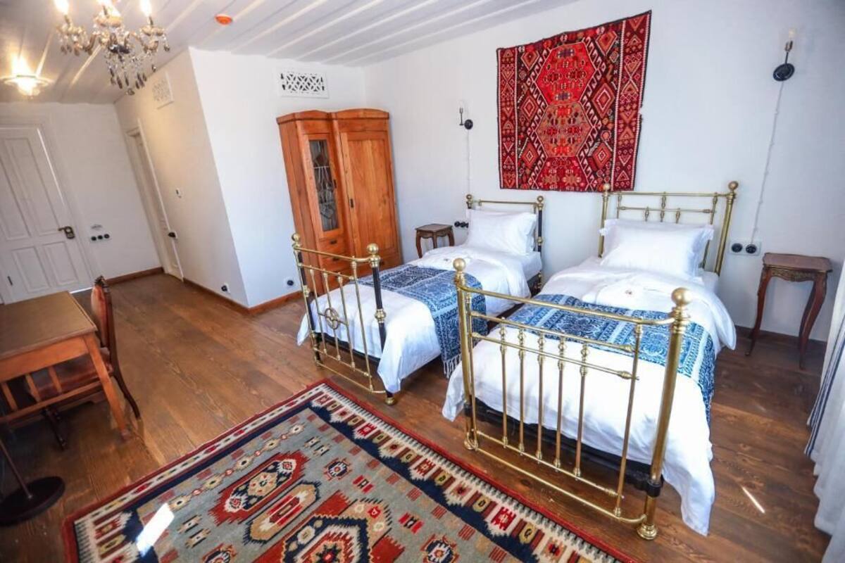 Una habitación con dos camas, un armario de madera, una araña y una alfombra estampada.
