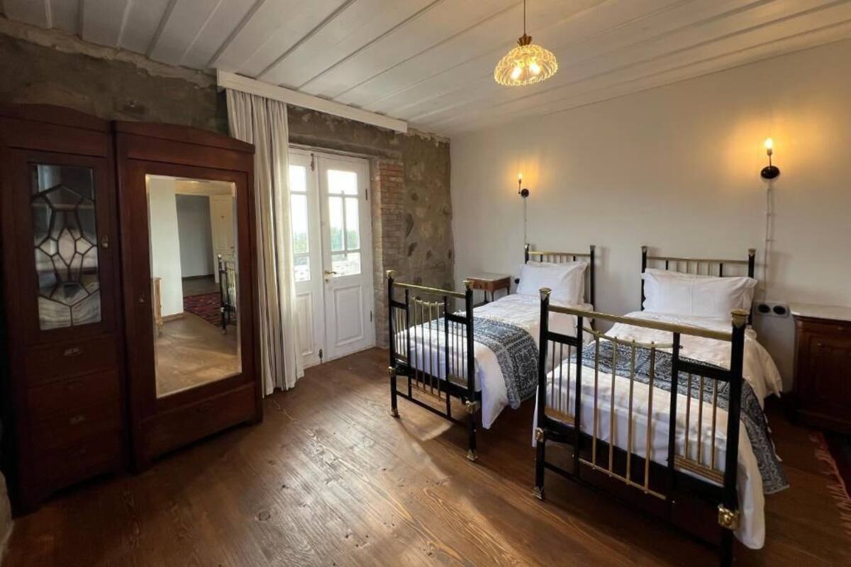Una habitación con dos camas, suelo de madera, un espejo grande y un techo rústico.