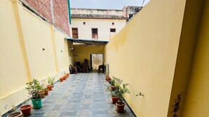 Un pasillo estrecho con suelo de baldosas, plantas en macetas a ambos lados y un suelo de madera al final.