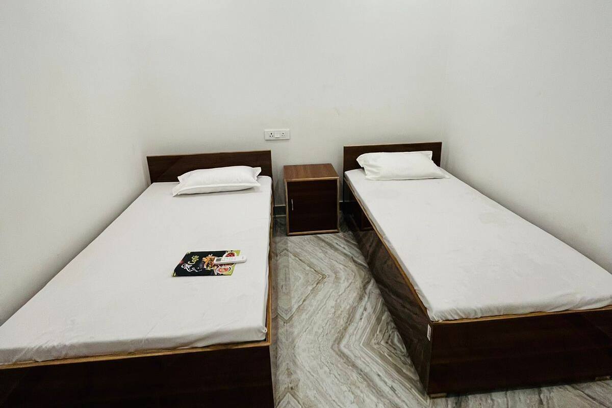 Una habitación con dos camas individuales, una mesita de noche de madera, suelo de mármol y una pared blanca con un equipo de aire acondicionado.
