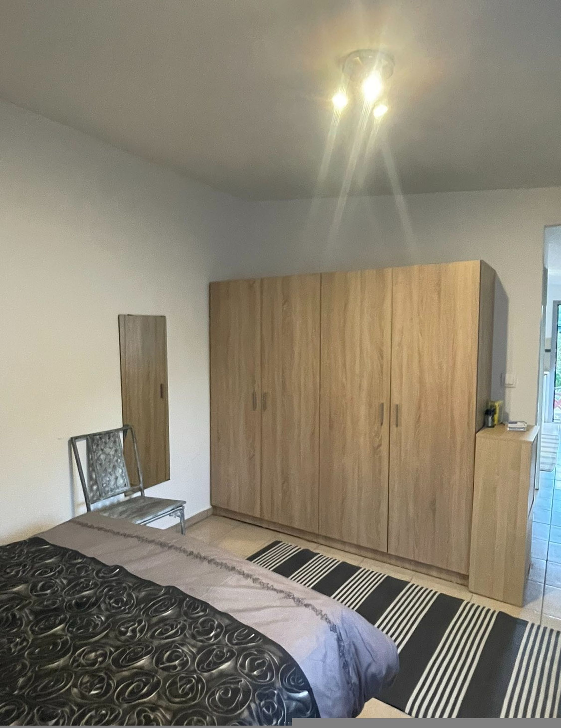 A bedroom with a bed, a wardrobe, a chair, and a small table.