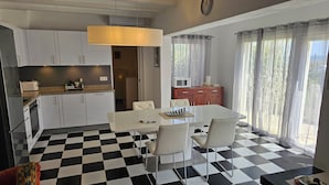 A modern kitchen with white cabinets, a black and white checkered floor, and a dining area with a white table and chairs. - Casa Playa Direct (Dénia)