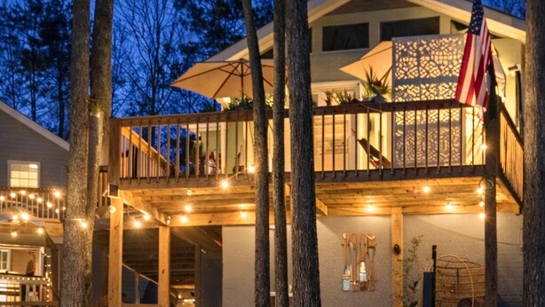 Una casa de dos pisos con balcón, terraza de madera y luces colgantes.
