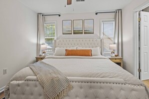 A bedroom with a large bed, two bedside tables, a window with curtains, and a door.