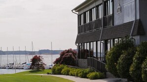 Un edificio frente al agua con balcón, césped y vista a barcos.