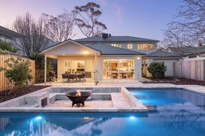 Une maison moderne dotée d’une piscine, d’un patio avec mobilier d’extérieur et d’un foyer.