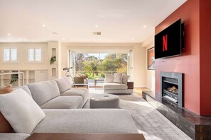 A modern living room with a sectional sofa, a fireplace, and a TV mounted on a red wall. - The Nepean | 100m to Beach, Pool & Fire Pit (McCrae)