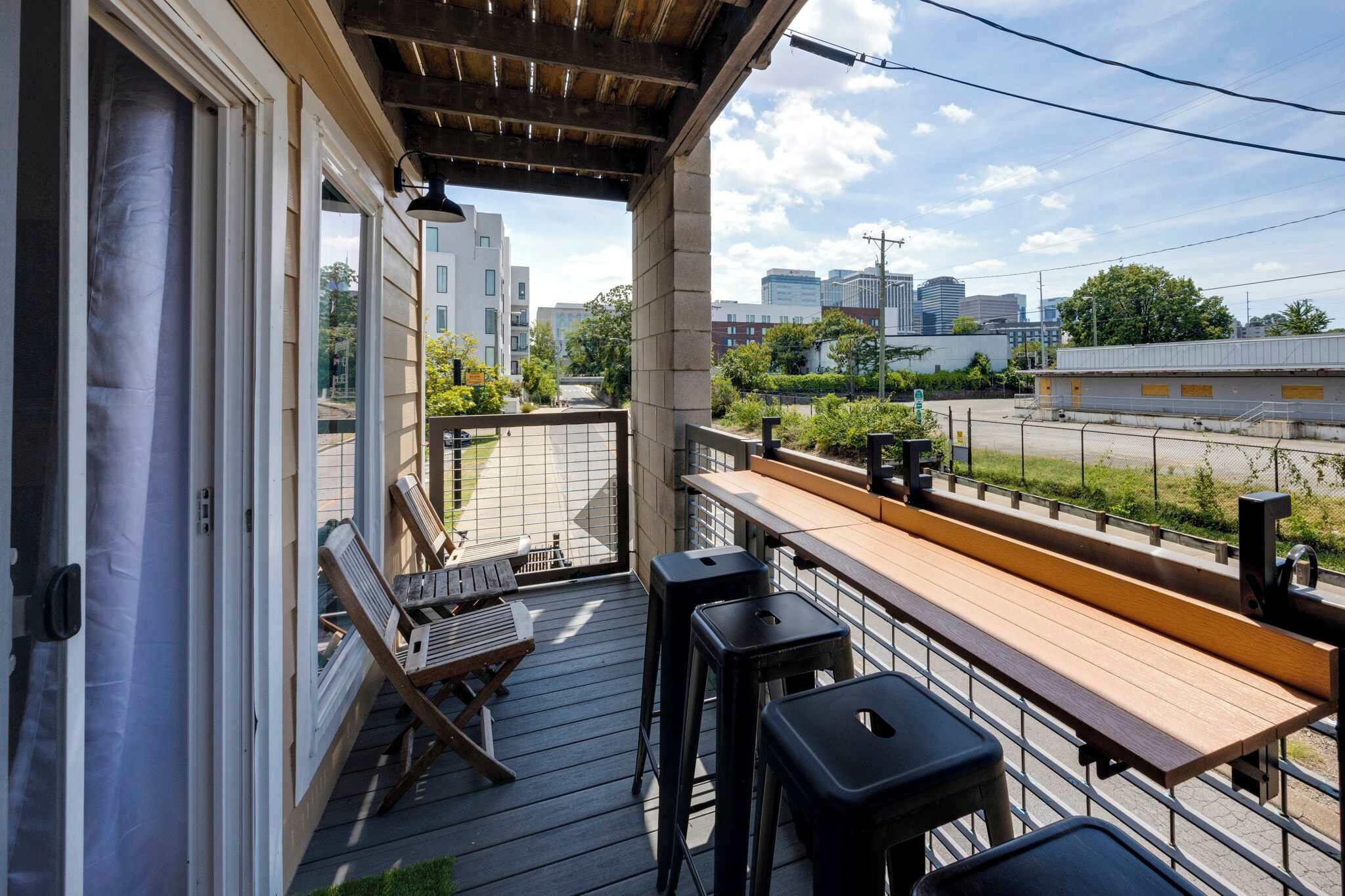 Un balcon doté d’une terrasse en bois, d’une table et de deux tabourets de bar.