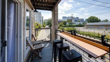 Un balcon doté d’une terrasse en bois, d’une table et de deux tabourets de bar.