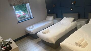 Habitación de hotel con dos camas individuales, un escritorio pequeño, una ventana con vista a vegetación y una pared de acento azul oscuro.