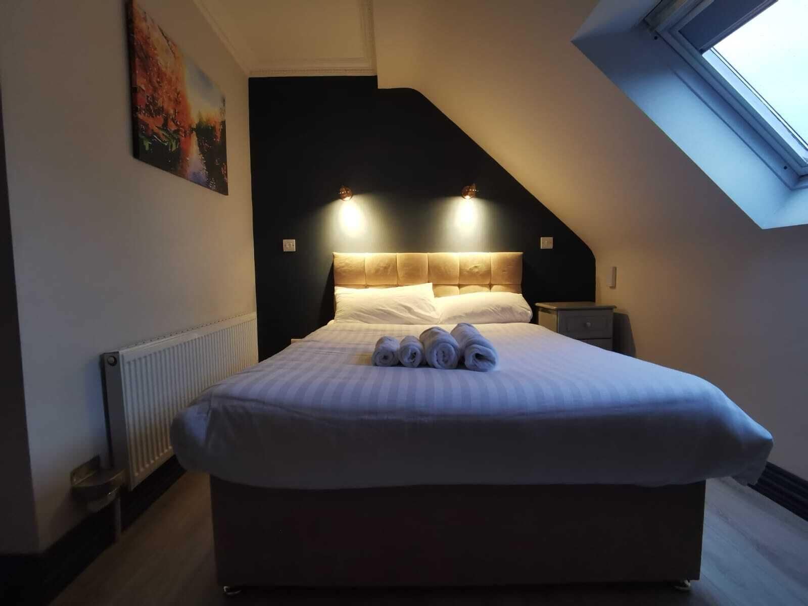 Un lit bien fait, avec des serviettes pliées, une tête de lit sombre et une lucarne au-dessus.