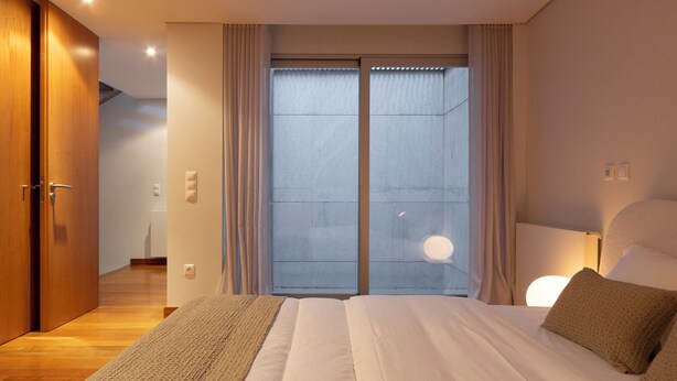 Ein modernes Hotelzimmer mit einem großen Bett, einem Holzschrank, einer Schiebetür zum Balkon und einem Nachttisch mit einer Lampe.