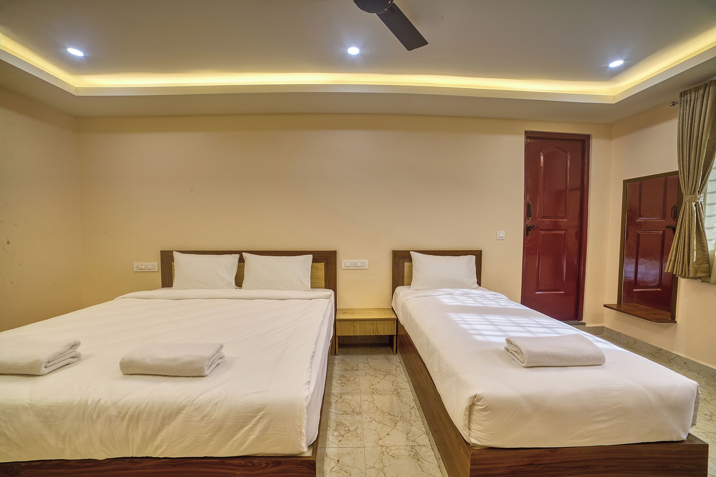 A hotel room with two beds, a ceiling fan, recessed lighting, a wooden door, and a window with curtains.