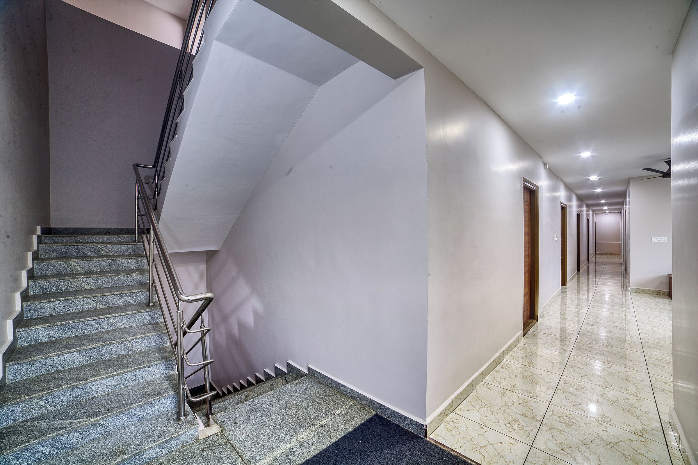 A modern hotel interior with a marble staircase, a straight hallway, and a ceiling fan.