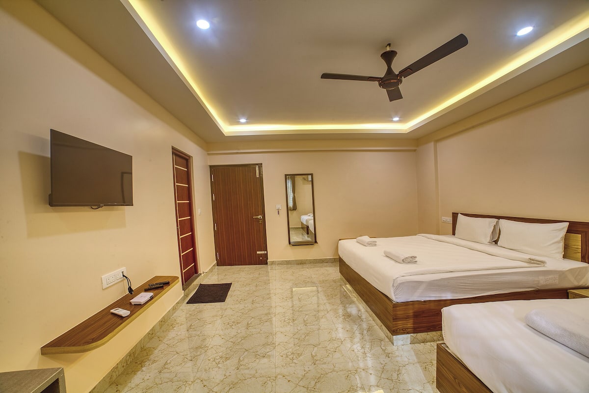 Una habitación de hotel con una cama, una mesita de noche, un espejo, un ventilador de techo y un televisor montado en la pared.