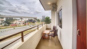Un balcón con mesa y sillas, con vista a una calle concurrida y edificios.