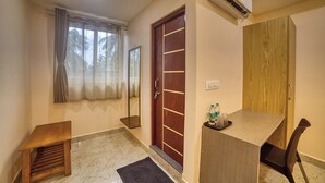 Habitación de hotel con un escritorio de madera, una silla, una mesita, un espejo, una puerta y un equipo de aire acondicionado.