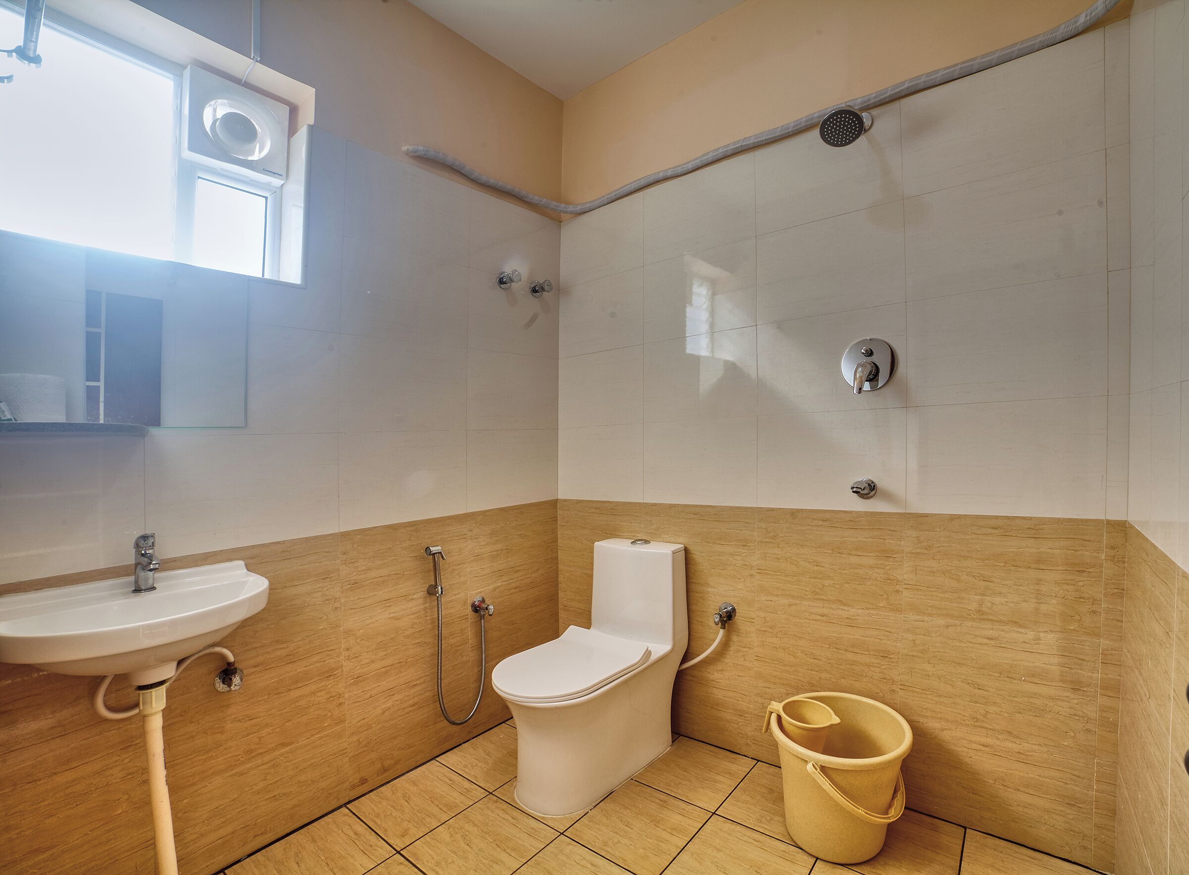 A bathroom with a sink, toilet, shower, and a bucket.