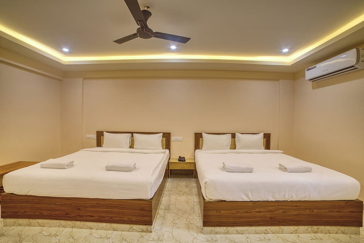 Habitación de hotel con dos camas, cabeceros de madera, ropa de cama blanca, ventilador de techo, luces empotradas, unidad de aire acondicionado y piso de mármol.