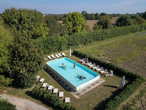 An outdoor swimming pool surrounded by lounge chairs and umbrellas, with a view of the countryside.